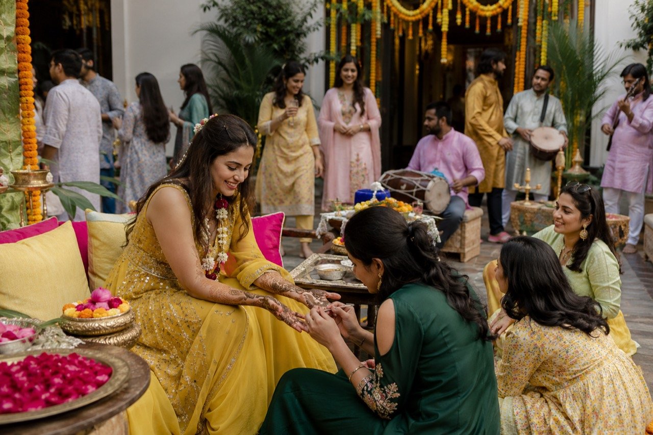 A festive Indian mehendi celebration with marigold garlands, warm lighting and family members gathered around a bride-to-be having henna applied to her hands