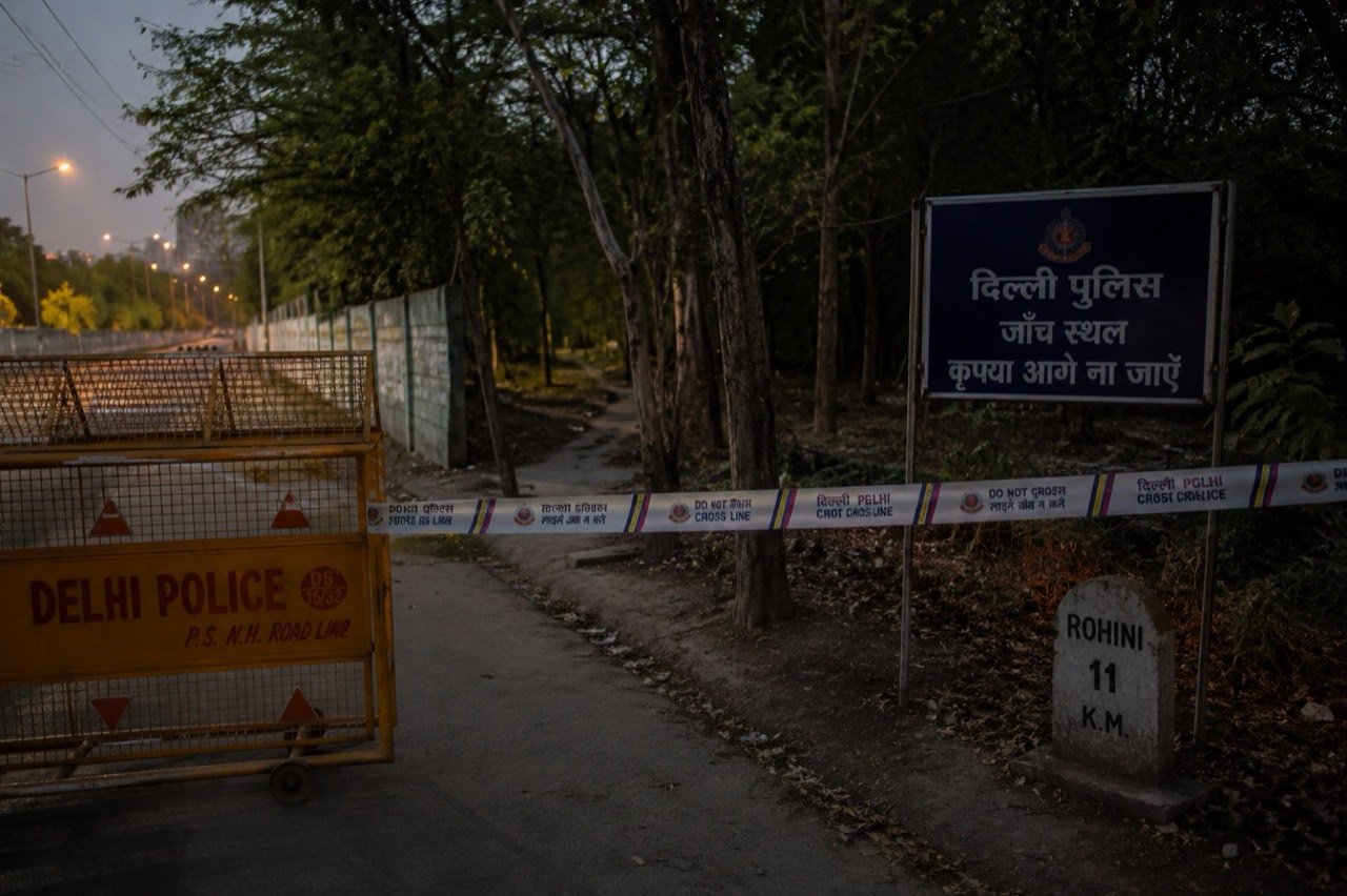 A Delhi street at night where homeless families sleep on footpaths near a market corridor