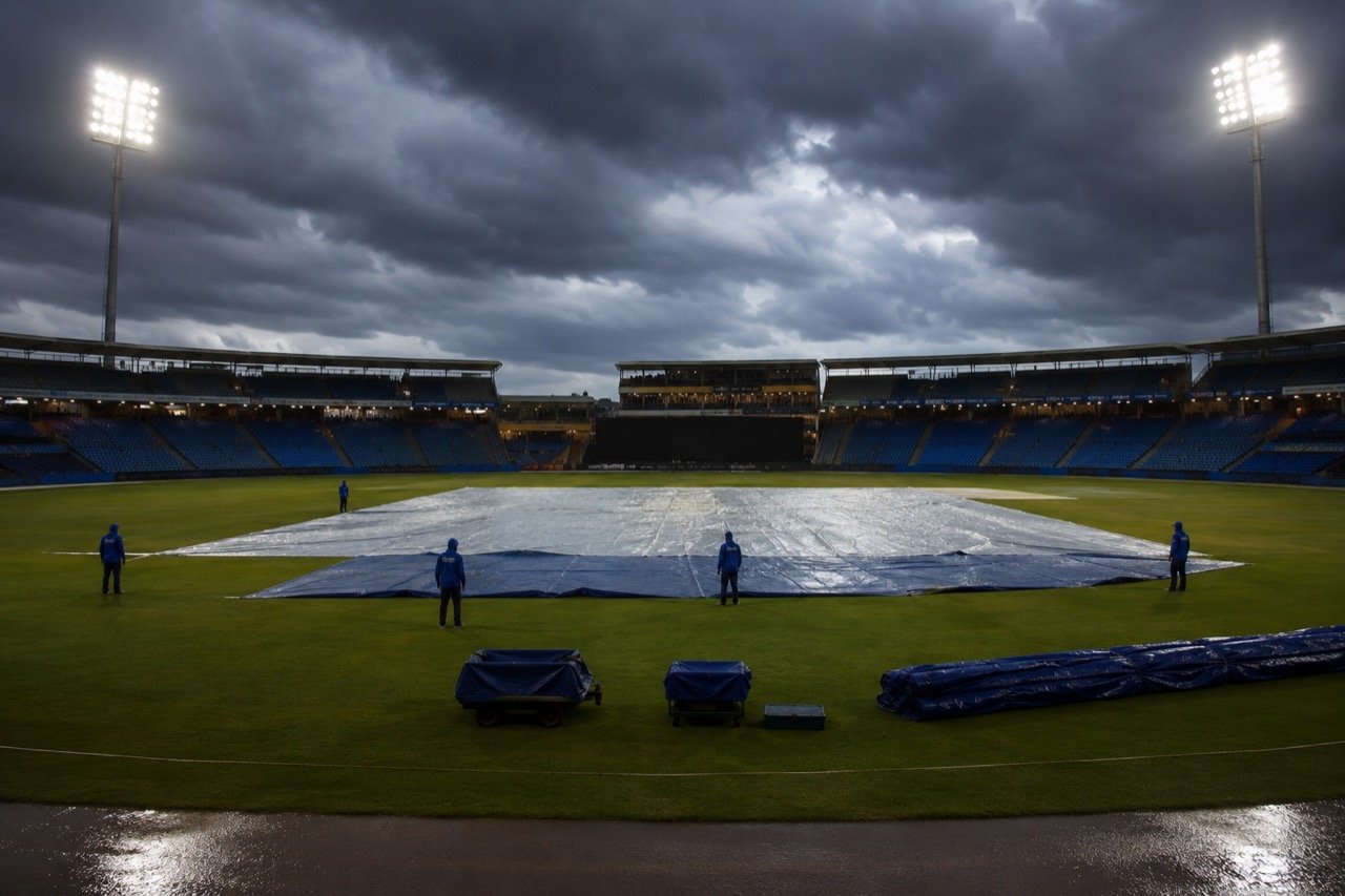 Dark rain clouds gathering over a floodlit cricket stadium as groundstaff stand ready with covers before an India-England T20I