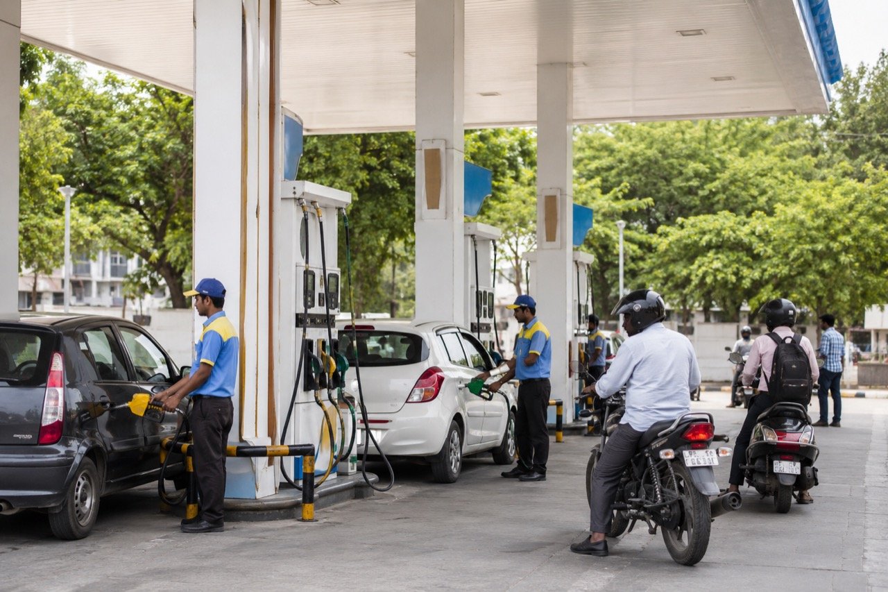 A busy Indian petrol pump at dusk with cars and two-wheelers queuing at fuel dispensers under bright forecourt lighting