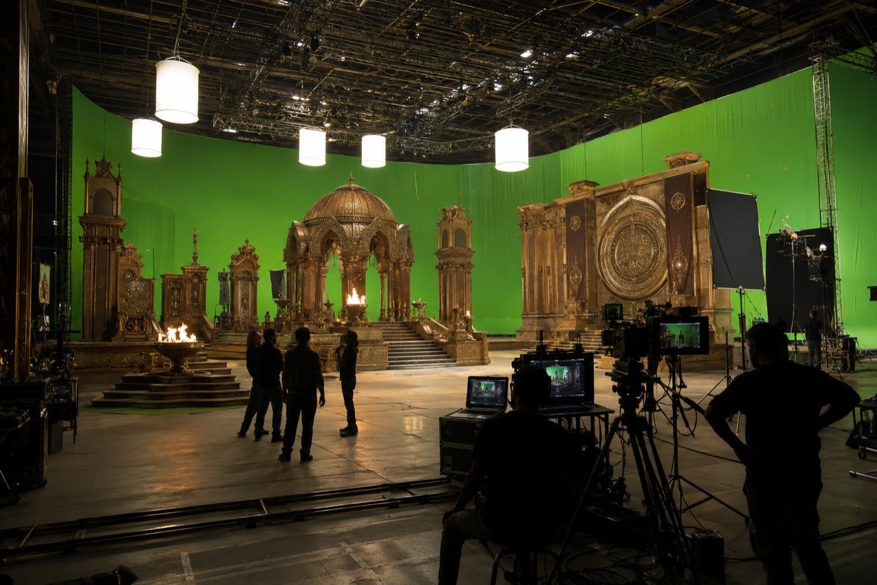 A vast film studio set with towering epic-scale scenery, camera cranes and crew at work, evoking the large-scale production of a multi-part Indian cinematic epic.