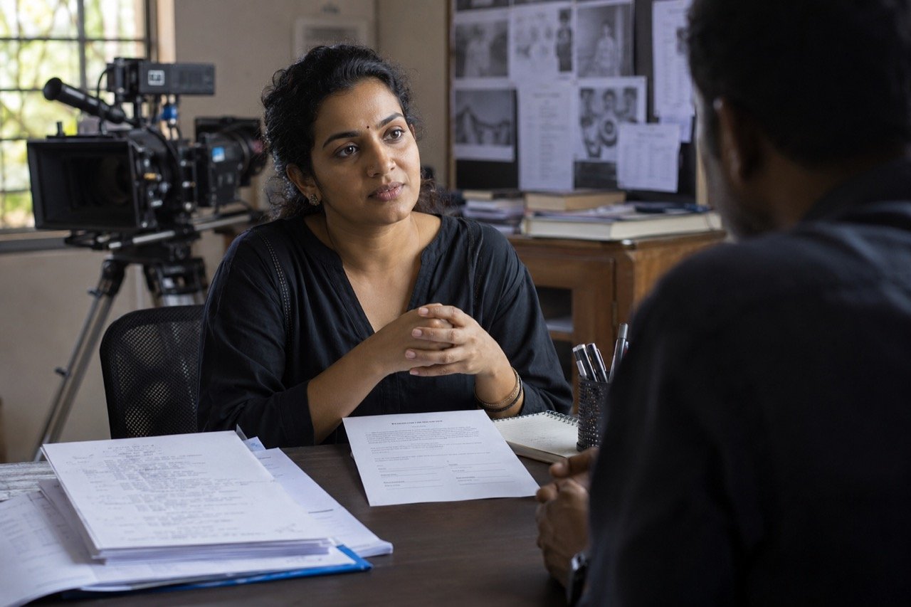 A young actor signs a film contract on a busy Malayalam movie set, with cameras and crew visible in the background