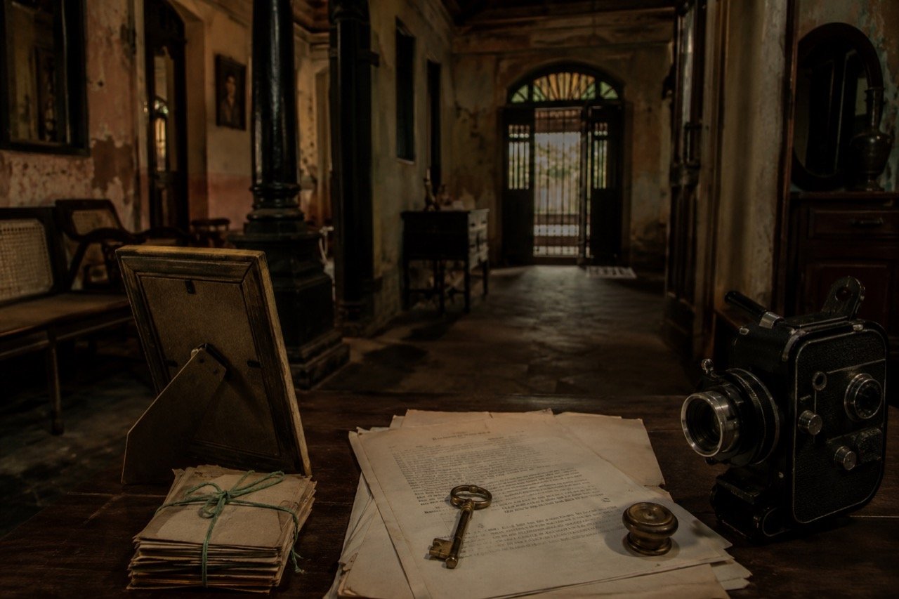 An old ancestral Indian mansion at dusk with family members gathered tensely around heirlooms and property documents in a dim hall